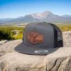 deer hunting trucker cap with a leather patch on a rock with mountains in the background